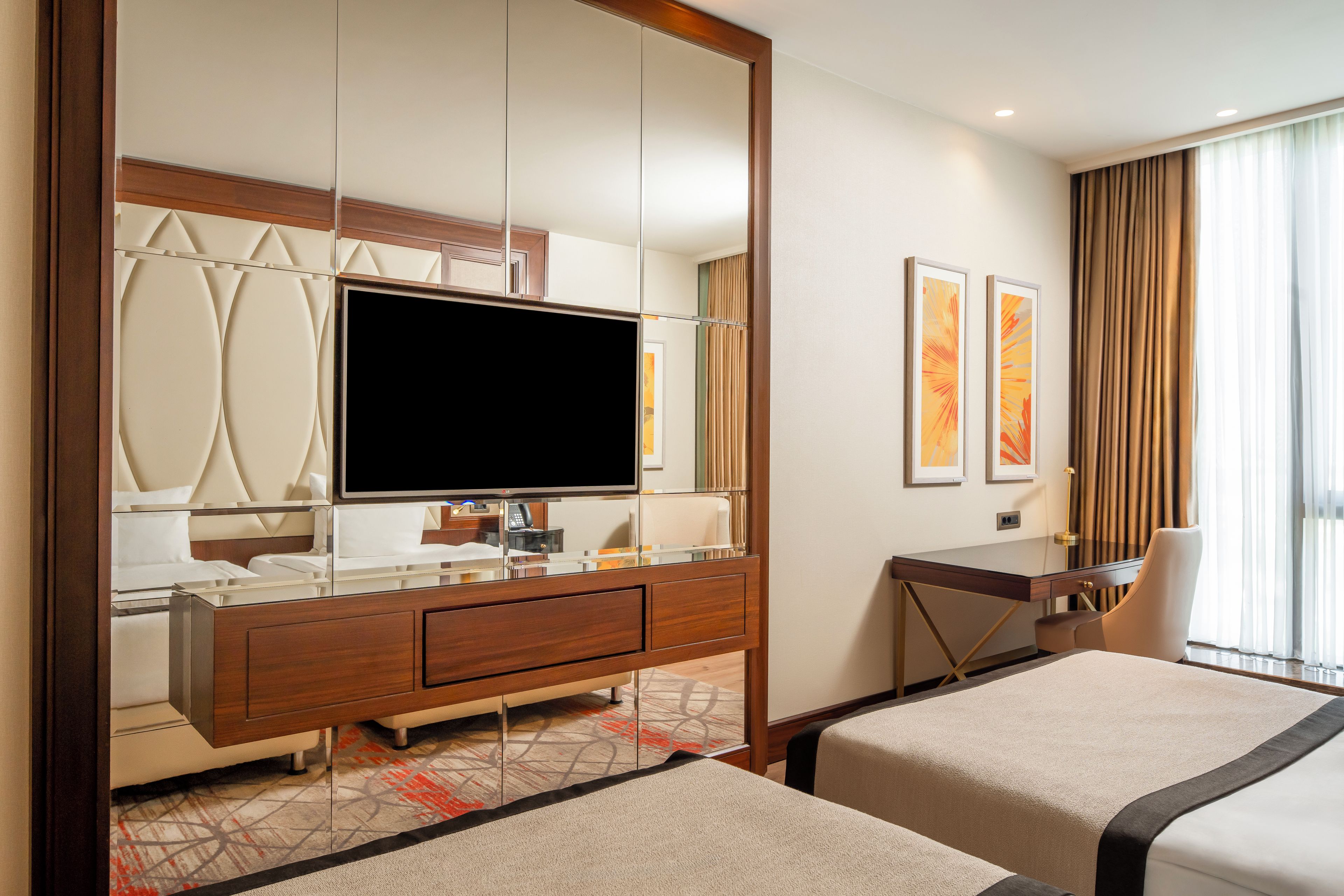 A hotel room with a large mirror, a flat-screen TV, a desk, two beds, and artwork on the wall.