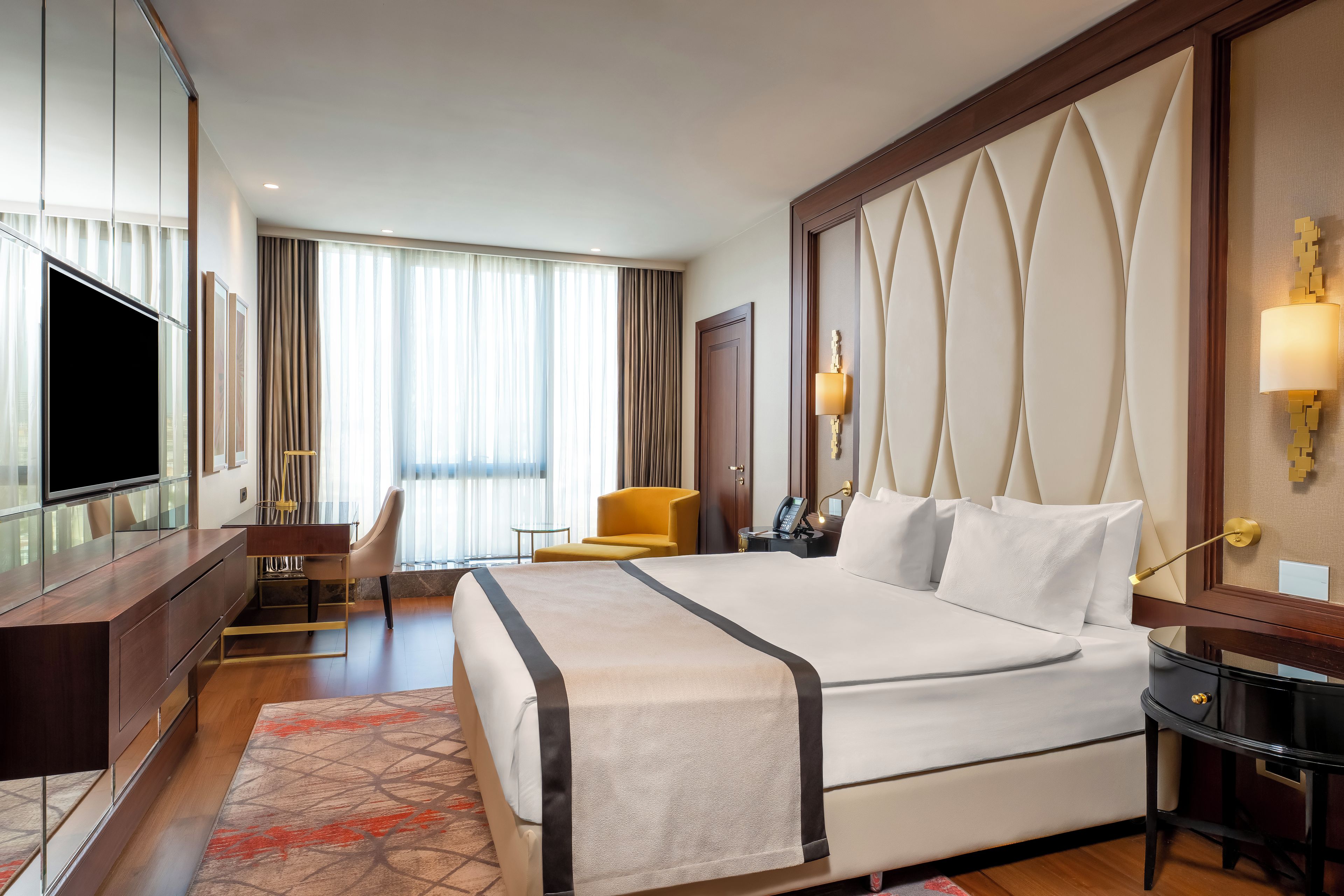 Una habitación de hotel con una cama grande, un escritorio con silla, un televisor y una mesita de noche con lámpara.