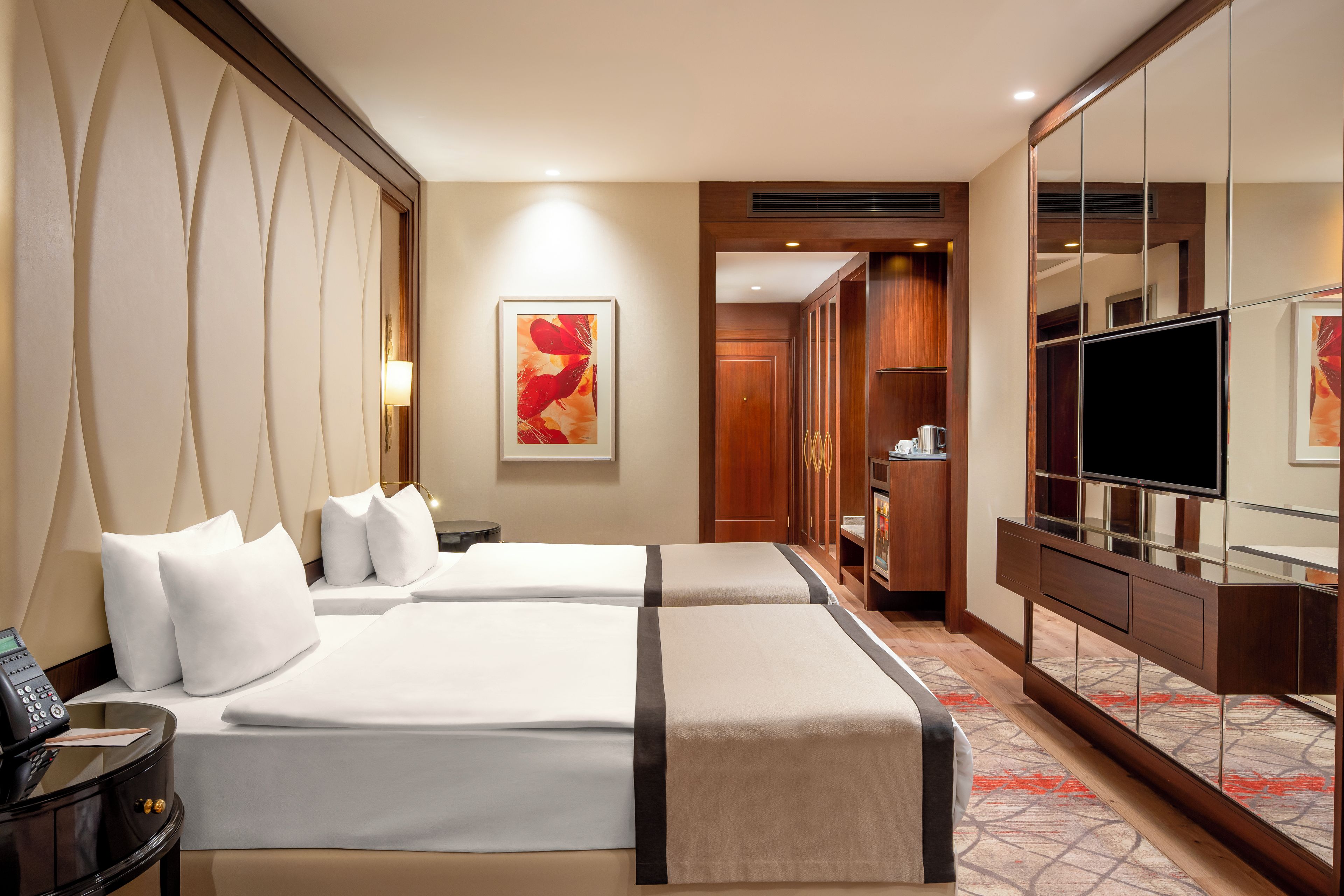 A hotel room with two beds, a TV, a wardrobe, and a painting on the wall.