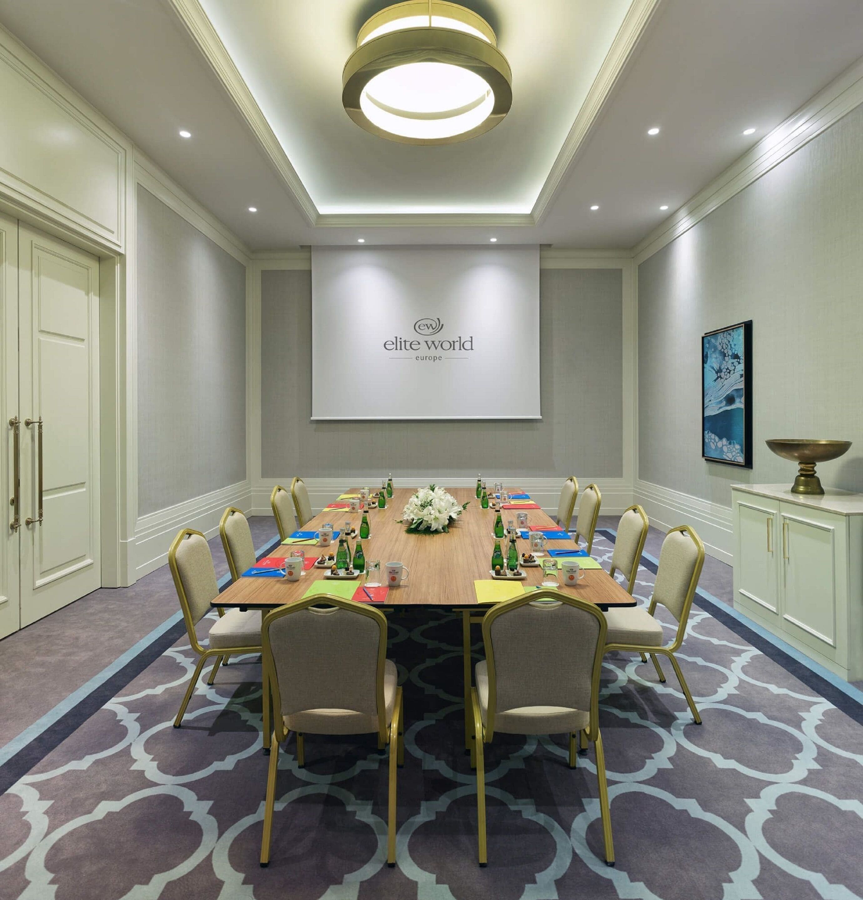 A conference room with a long table, chairs, and a projector screen displaying "elite world europe".