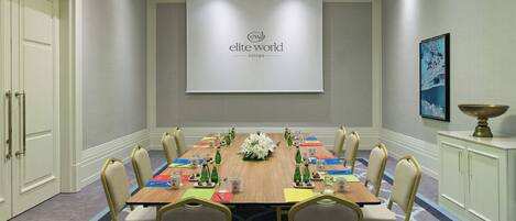 A conference room with a long table, chairs, and a projector screen displaying "elite world europe".