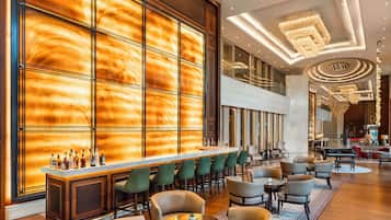 A modern hotel lobby with a bar area, seating, and a grand chandelier.