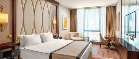 A hotel room with a large bed, a desk, a chair, and a TV.