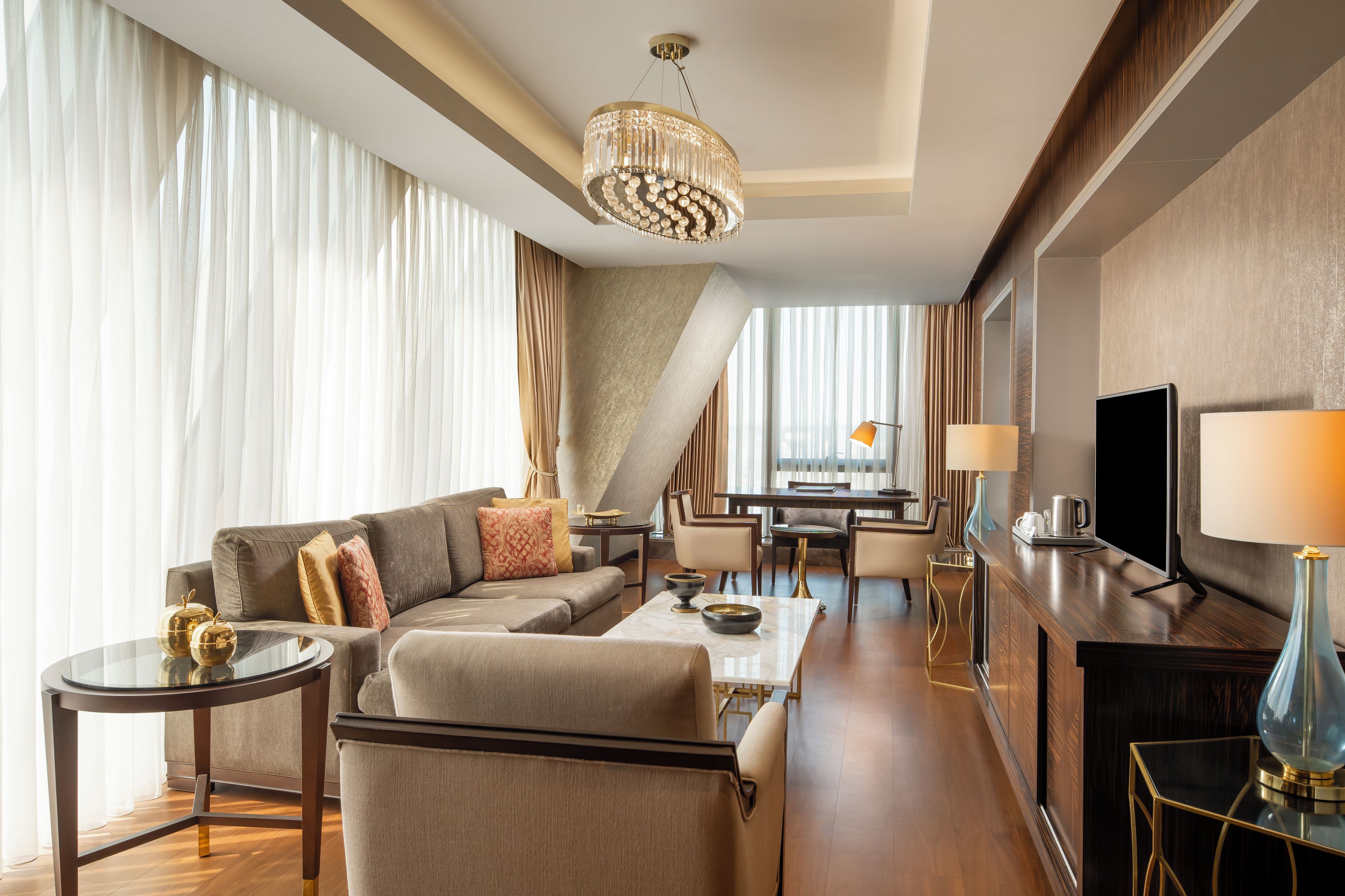 A modern hotel room with a sofa, coffee table, TV, and a dining area.