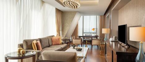 A modern hotel room with a sofa, coffee table, TV, and a dining area.