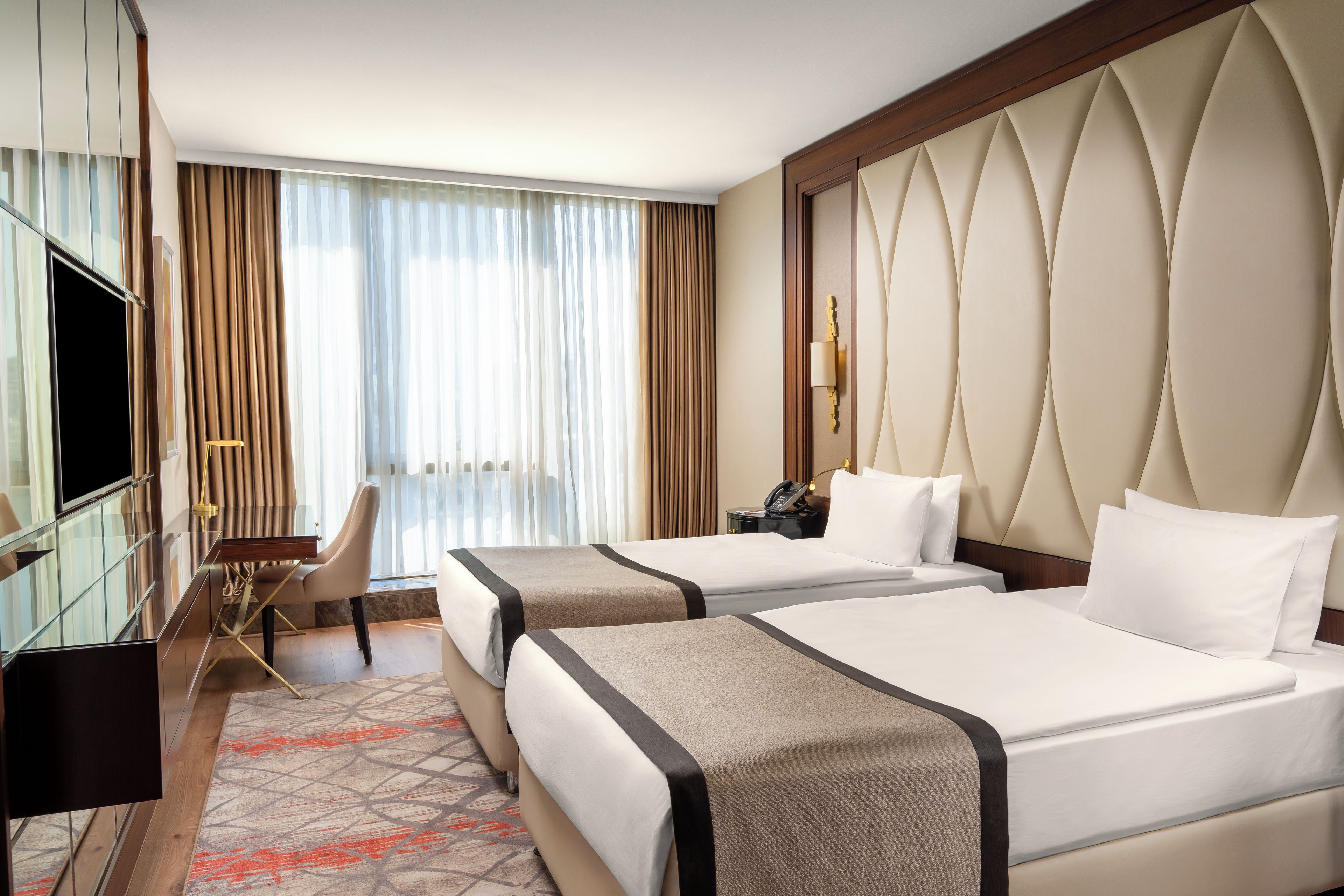 A hotel room with two beds, a desk, a chair, and a television.