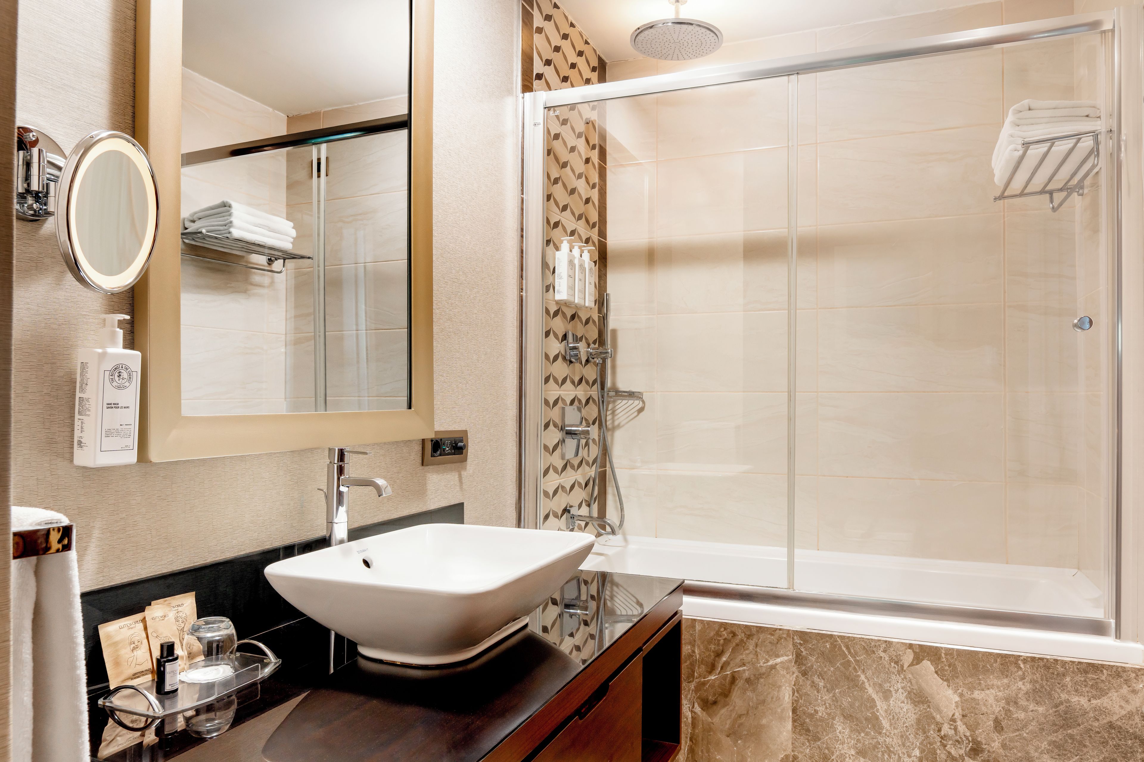 A modern bathroom with a large mirror, a vessel sink, a shower with a glass door, and a towel rack.