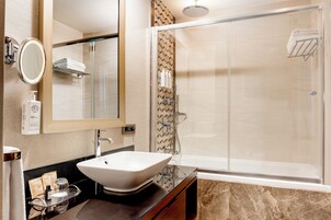 A modern bathroom with a large mirror, a vessel sink, a shower with a glass door, and a towel rack.