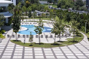 Zona de piscina con tumbonas y árboles, bordeada por un camino pavimentado.