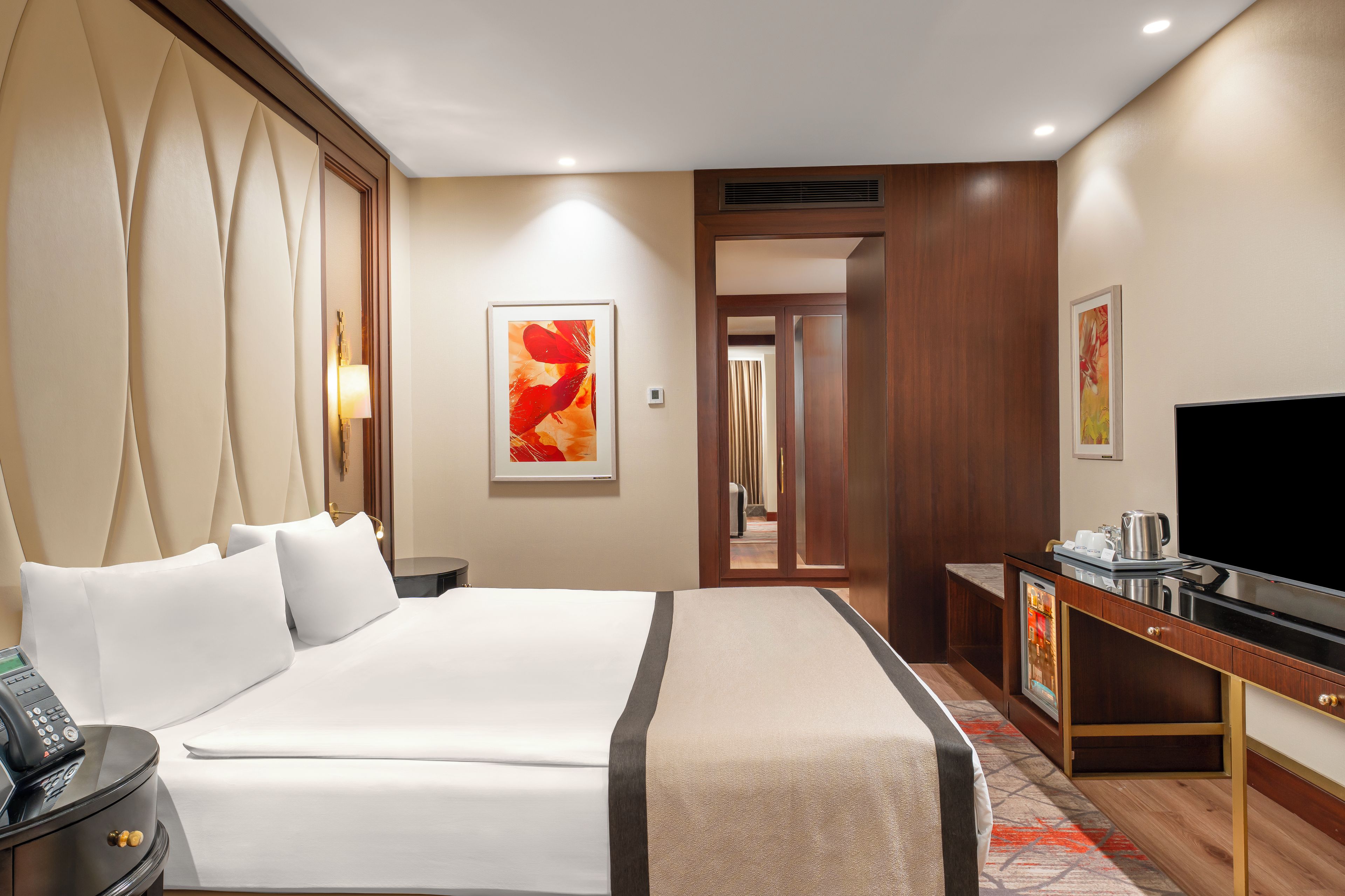 A hotel room with a large bed, a desk with a television, and a bathroom visible through an open door.