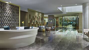 Un moderno vestíbulo de hotel con mostrador de recepción, zona de estar y gimnasio con paredes de vidrio.