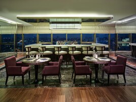 Un restaurante de altura con vistas panorámicas de la ciudad, que incluye una zona de bar con diversas opciones de asientos y una decoración interior moderna.