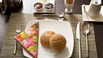Uma mesa posta para o café da manhã, com dois pães, uma xícara de café e acompanhamentos.
