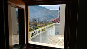 Une vue depuis une fenêtre ornée d’une rambarde en métal, donnant sur une ville avec une tour imposante et des montagnes en arrière-plan.