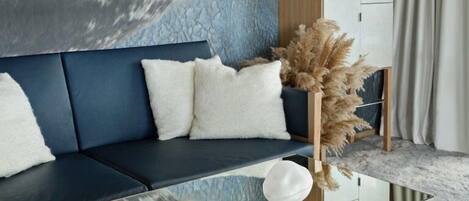 Una sala de estar moderna con una mesa de centro de vidrio, un sofá azul oscuro, cojines blancos y una planta decorativa.