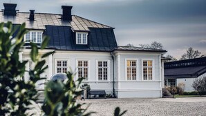 En vit byggnad med ett svart tak, en stenlagd innergård och en bänk.