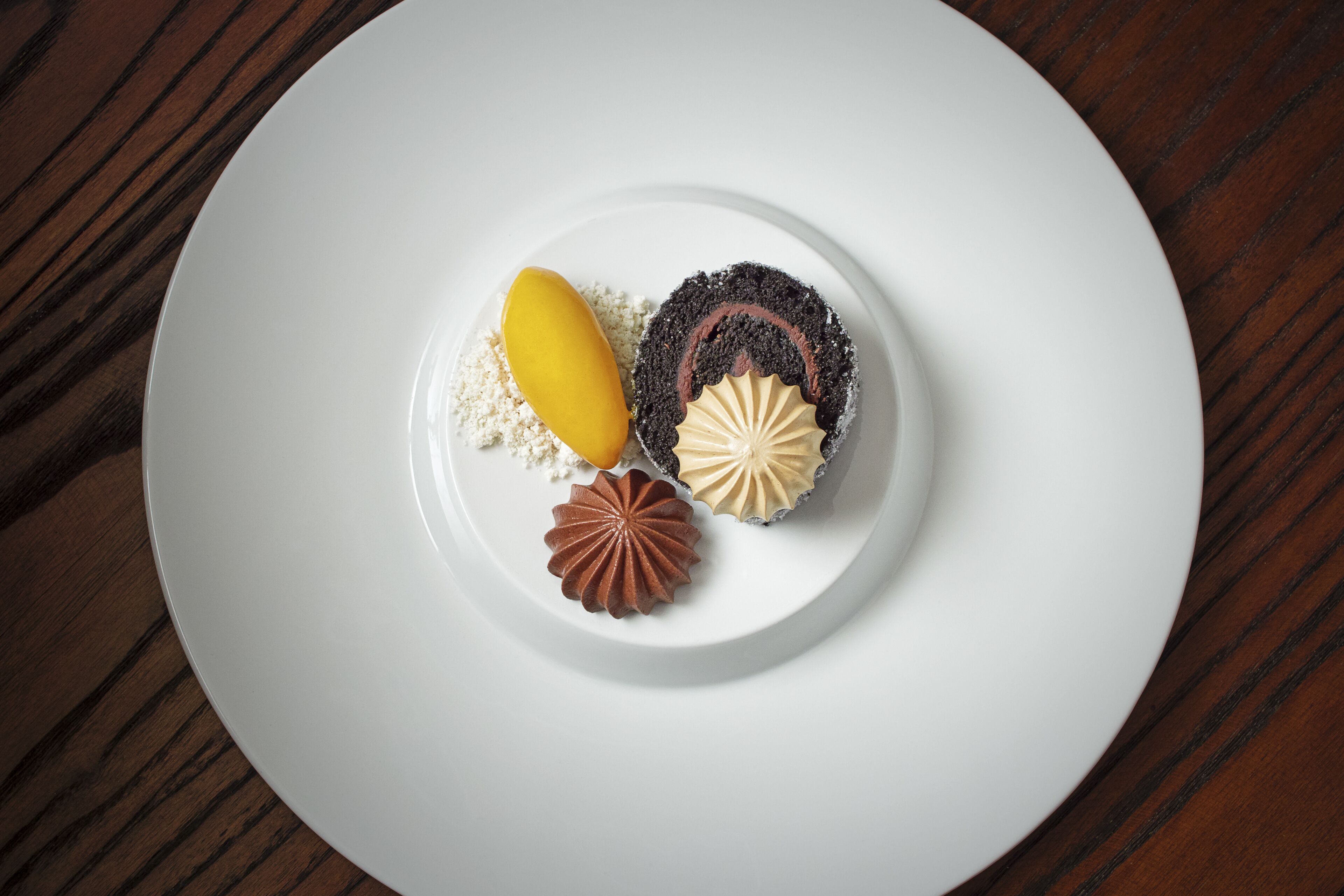 Une assiette blanche avec trois desserts, posée sur une table en bois.