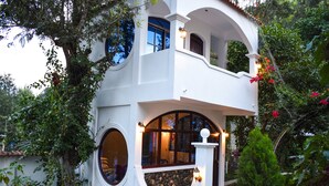 Un edificio de dos pisos con fachada blanca, ventanas amplias y un balcón con barandilla de piedra.