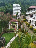 Un edificio de varios pisos con balcones, rodeado de abundante vegetación y un jardín con flores rosadas.