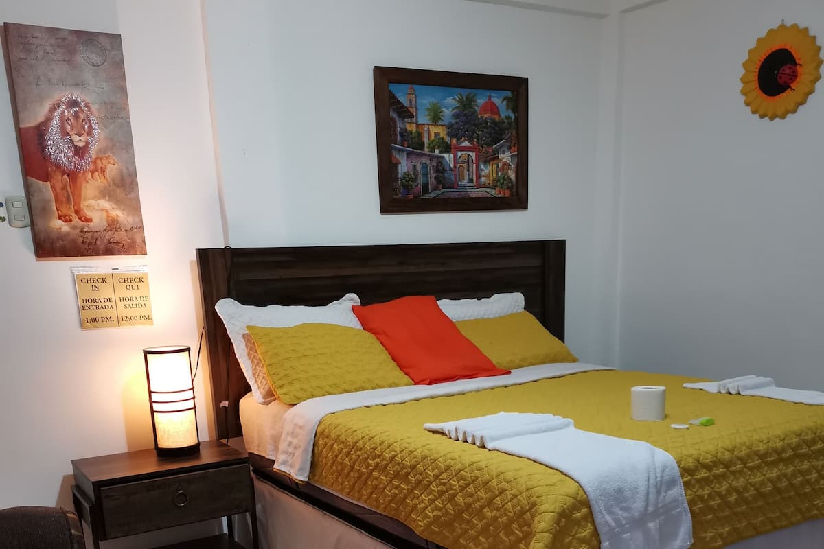 Une chambre à coucher bien rangée, avec un lit, une table de chevet, une chaise et une œuvre d’art accrochée au mur.
