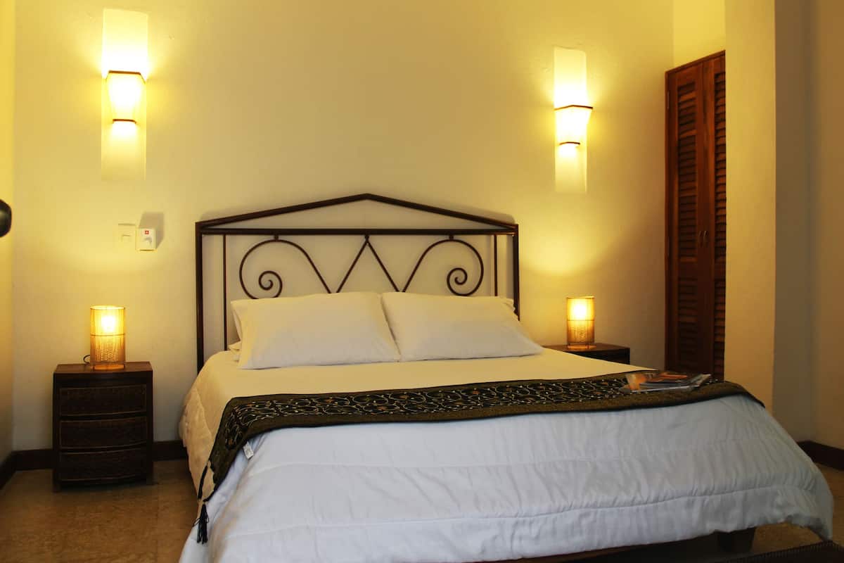 A neatly made bed with a metal headboard, two bedside lamps, and a wooden door on the right.