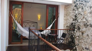 A balcony with a hammock, a bed, and a stone wall.