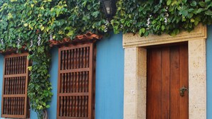 A building with a blue facade, two wooden windows with decorative grills, and a wooden door with a metal handle.