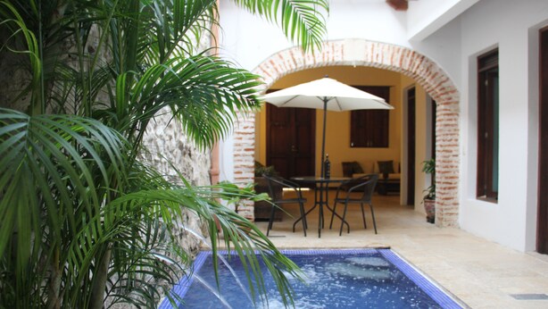 An outdoor pool area with a brick wall, a table and chairs, and a large umbrella.