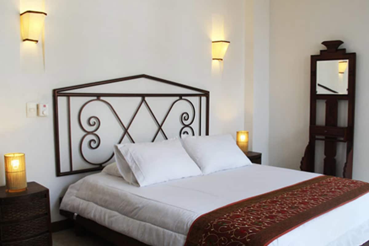 A neatly made bed with white linens and a red decorative throw, two bedside lamps, and a mirror on the wall.