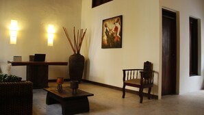 A room with a wooden bench, a chair, a table, a vase with sticks, and a painting on the wall.