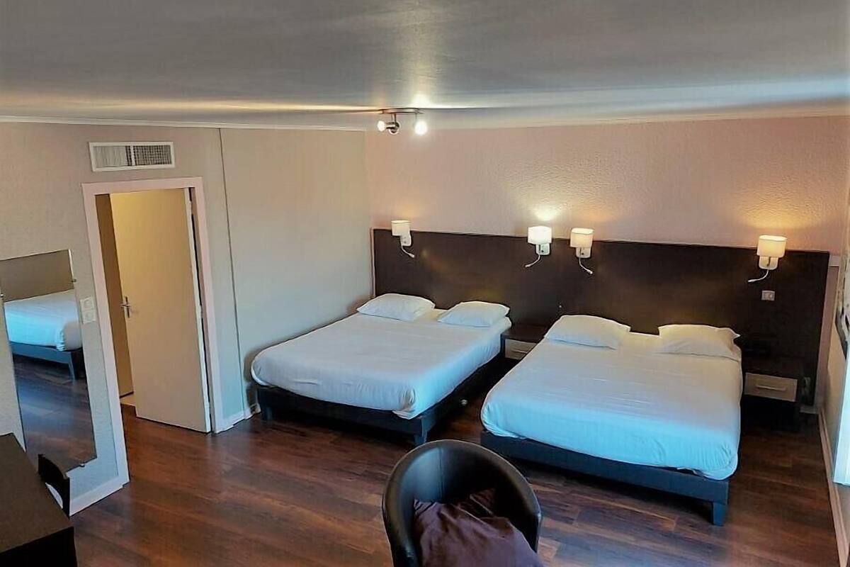A hotel room with two single beds, a small table, a chair, and a door leading to another room.