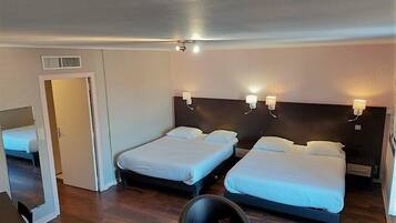 Een hotelkamer met twee eenpersoonsbedden, een klein tafeltje, een stoel en een deur die naar een andere kamer leidt.
