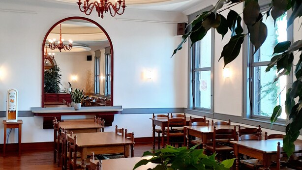 A dining area with wooden tables and chairs, a chandelier, and large windows. - Hôtel Le Château (Tournon-sur-Rhone)