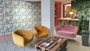 A cozy living area with a floral wallpaper, a wooden coffee table, two mustard-colored chairs, a pink sofa, and a kitchen area with a bamboo table and a coffee machine. - Hôtel Le Château (Tournon-sur-Rhone)