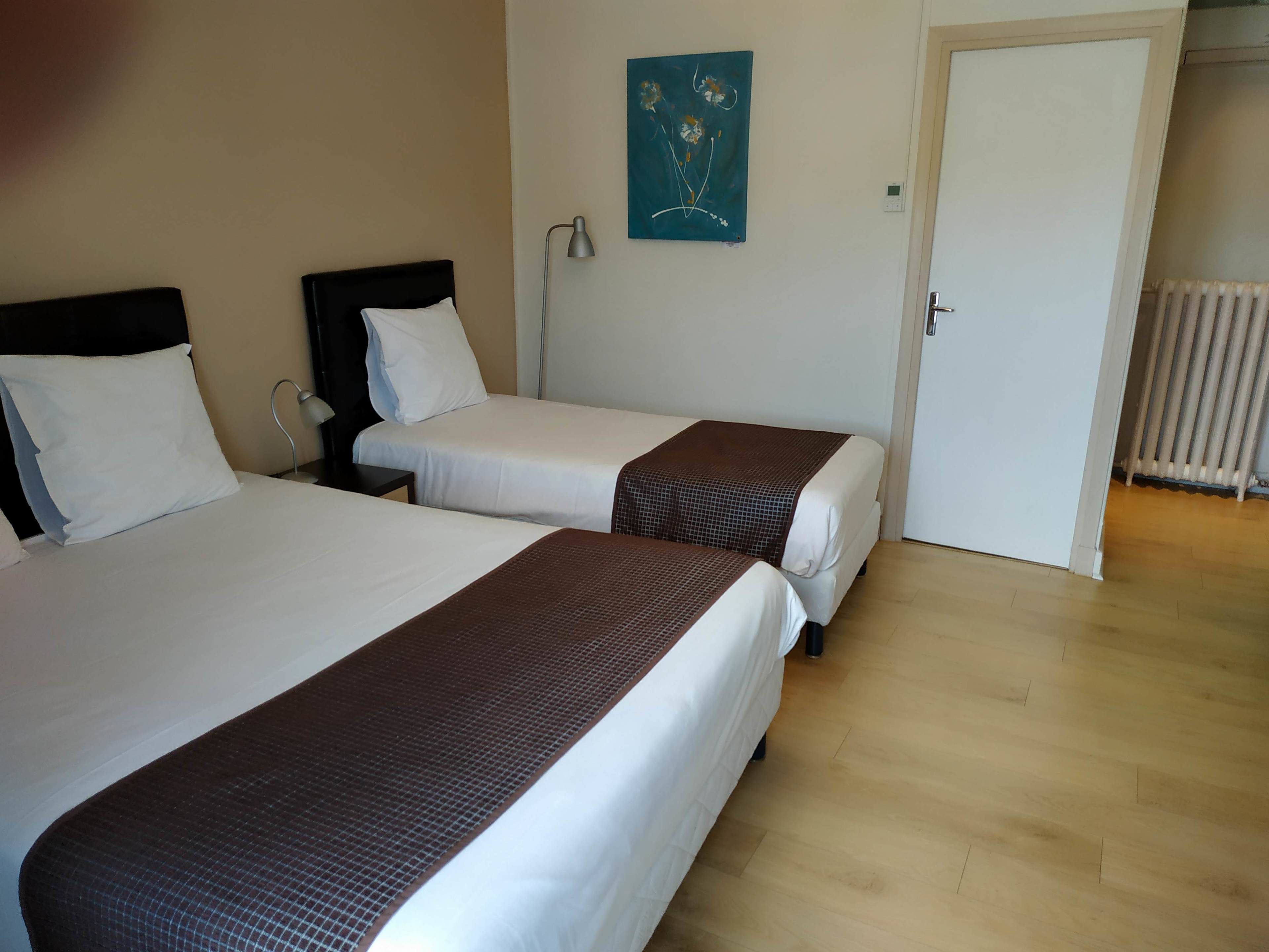 A hotel room with two beds, a painting on the wall, a lamp, and a radiator.