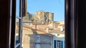 A view through a window of a building with a balcony, a stone structure in the background, and a parking sign. - Hôtel Le Château (Tournon-sur-Rhone)
