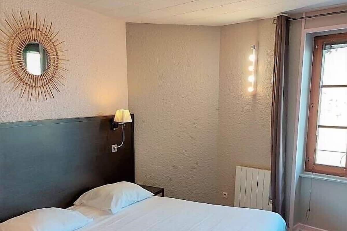 A hotel room with a large bed, a nightstand, a wall-mounted lamp, and a window with curtains.