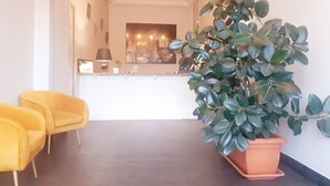 A modern interior with a reception desk, a large potted plant, and yellow chairs. - Hôtel Le Château (Tournon-sur-Rhone)