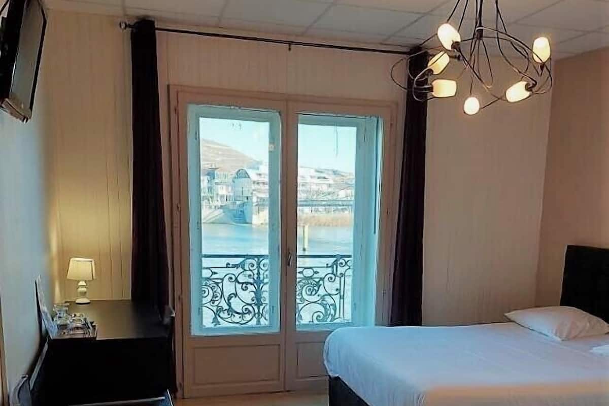 A hotel room with two beds, a desk, a chair, a TV, and a balcony with a view of buildings and a bridge.
