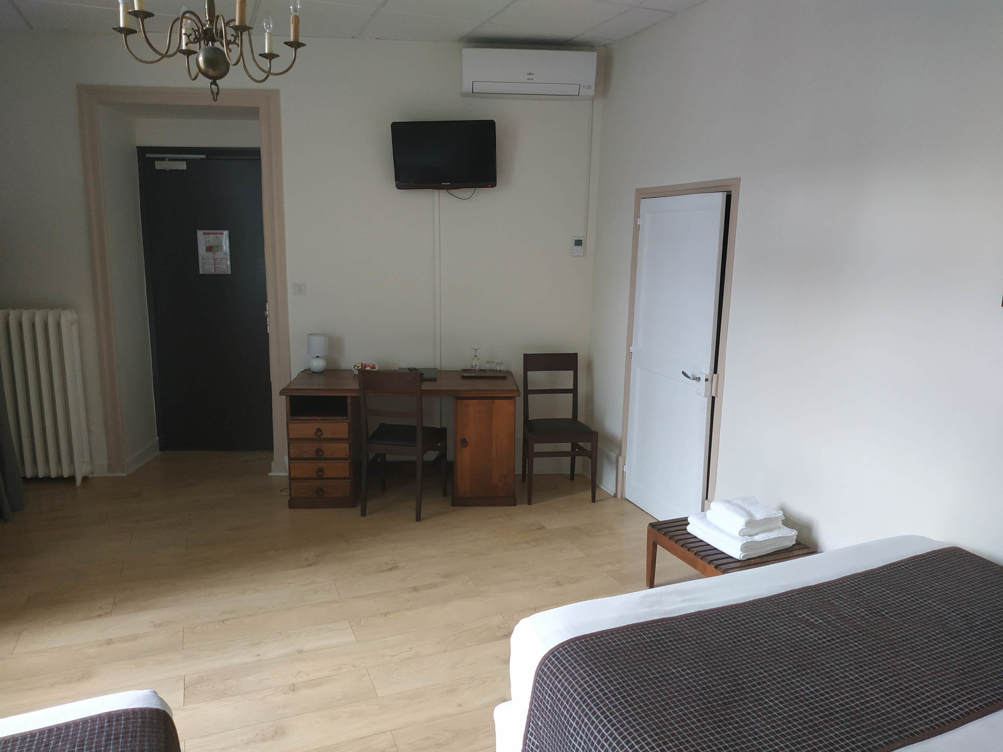 A hotel room with a wooden desk, two chairs, a bed, a TV, and a radiator.