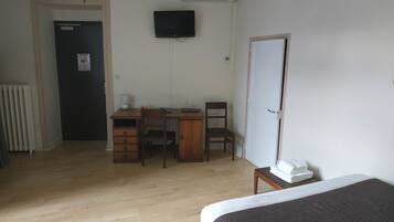 A hotel room with a wooden desk, two chairs, a bed, a TV, and a radiator.