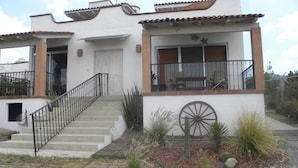 Uma casa de dois andares com escadas, varanda e um moinho decorativo.