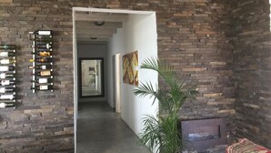 Ampla sala de estar com paredes de tijolo aparente, um corredor que leva a outro cômodo e uma lareira.