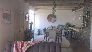 Uma sala de estar ampla com sofá, mesa de jantar com cadeiras, cozinha com balcão e parede de pedra.