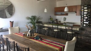 Cozinha moderna com parede de tijolos, bancadas de madeira e área de refeições com mesa e cadeiras de madeira.