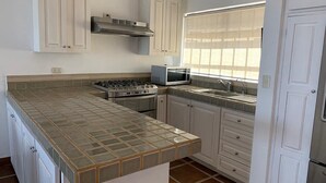 A kitchen with a central island, white cabinets, a microwave, a stove, and a window with blinds. - Casa Tulipan (San Miguel de Allende)