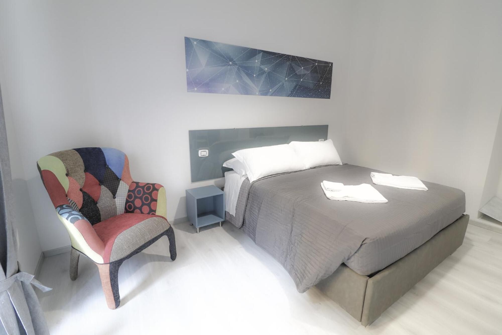 A modern bedroom with a large bed, a colorful armchair, and a wall art piece.