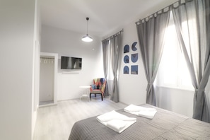 A modern bedroom with a bed, a chair, a TV, and curtains.