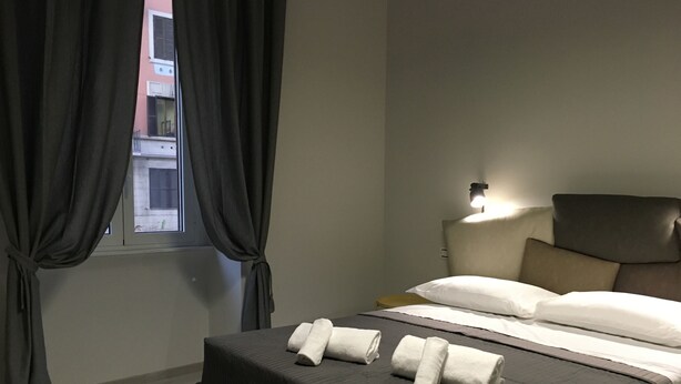 A hotel room with a bed, curtains, a nightstand, and a wall-mounted lamp. - Cinque Sogni (Rome)
