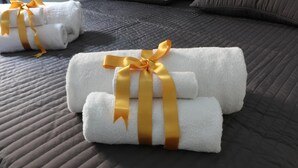 Neatly folded white towels with gold ribbons on a dark quilted bedspread. - Cinque Sogni (Rome)